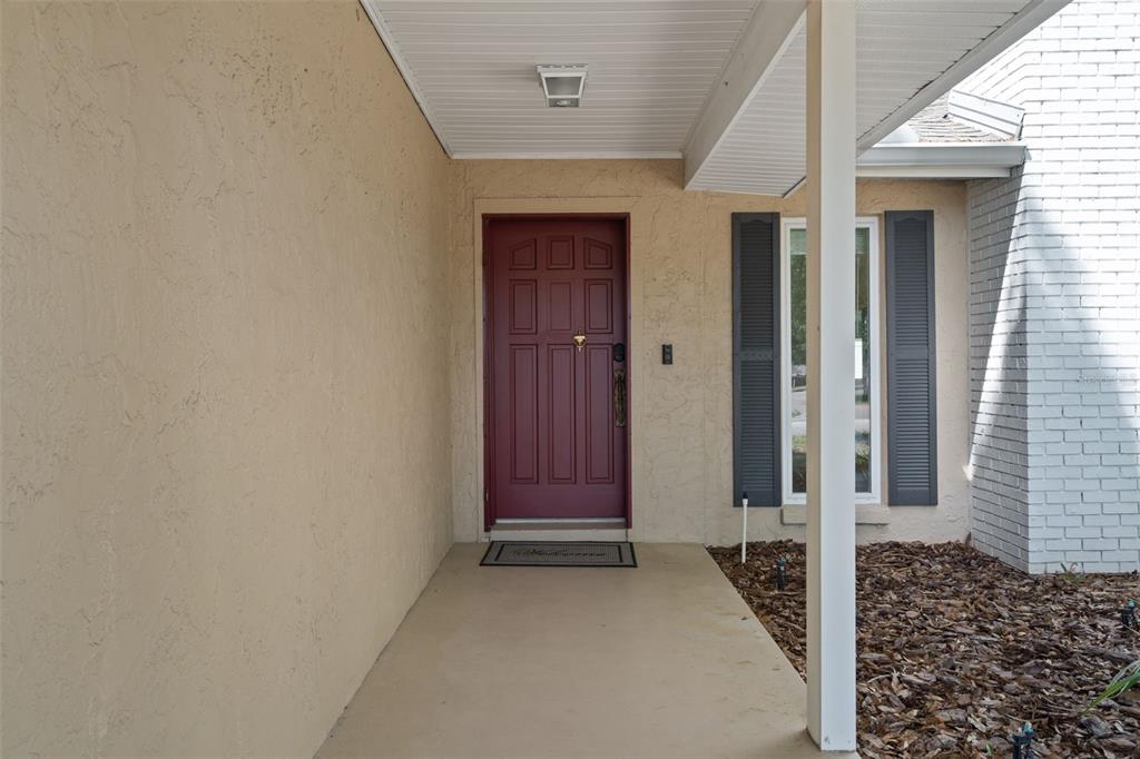 A covered entryway features a red front door, beige stucco walls, and a white post — 5519 FULMAR DRIVE, TAMPA, FL
