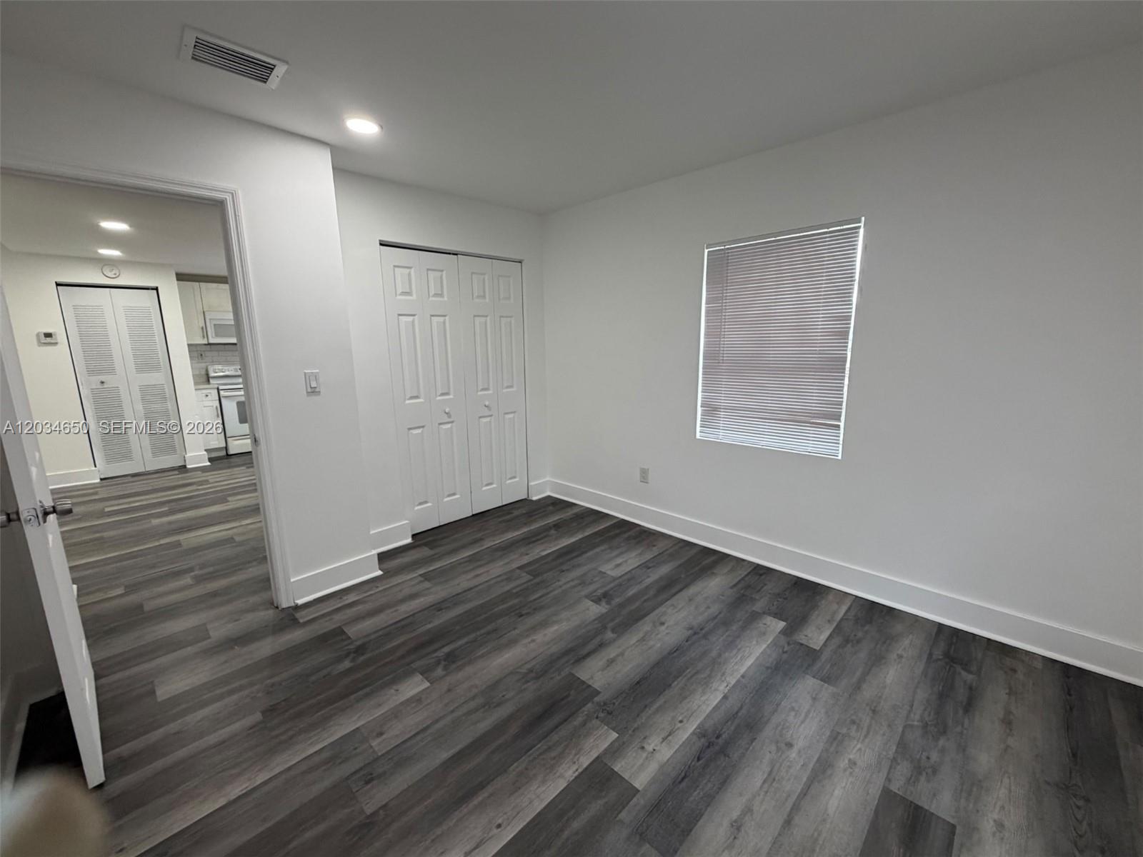 An empty room with gray wood-look flooring, white walls, a window, and a closet — 2025 NW 72nd St # 2, Miami FL 33147, MIAMI, FL