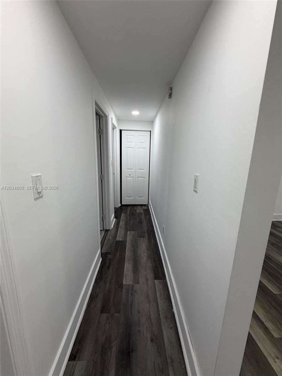 A narrow hallway features white walls, dark wood-look flooring, and a white bifold closet door — 2025 NW 72nd St # 2, Miami FL 33147, MIAMI, FL