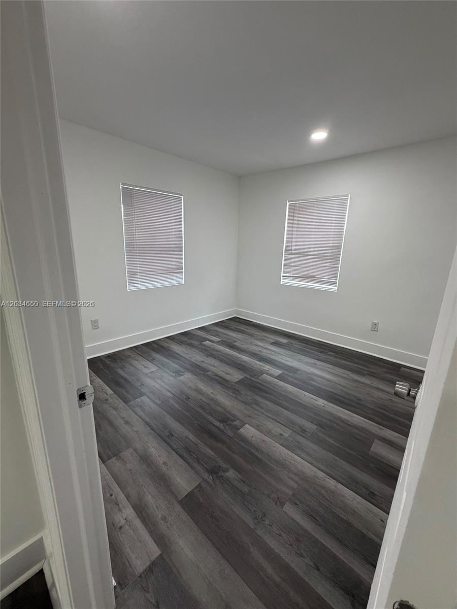 An empty bedroom features white walls, two windows with blinds, and dark wood-look flooring — 2025 NW 72nd St # 2, Miami FL 33147, MIAMI, FL