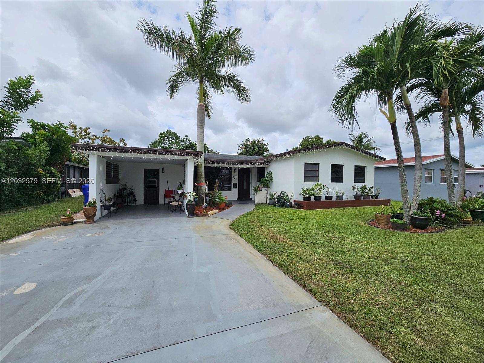 A single-story white house features a carport, a front lawn, and several palm trees — 7470 Polk St, Hollywood FL 33024, HOLLYWOOD, FL