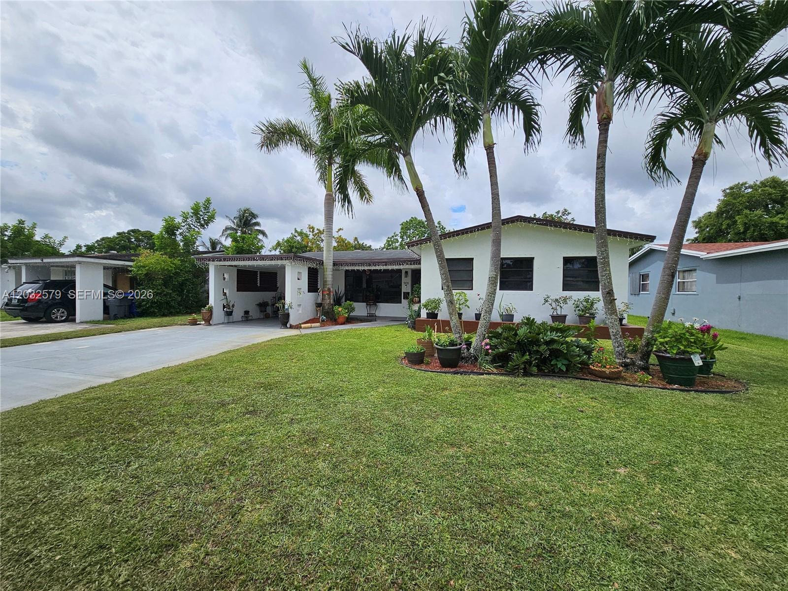 A single-story white house features a carport, palm trees, and a landscaped front yard — 7470 Polk St, Hollywood FL 33024, HOLLYWOOD, FL