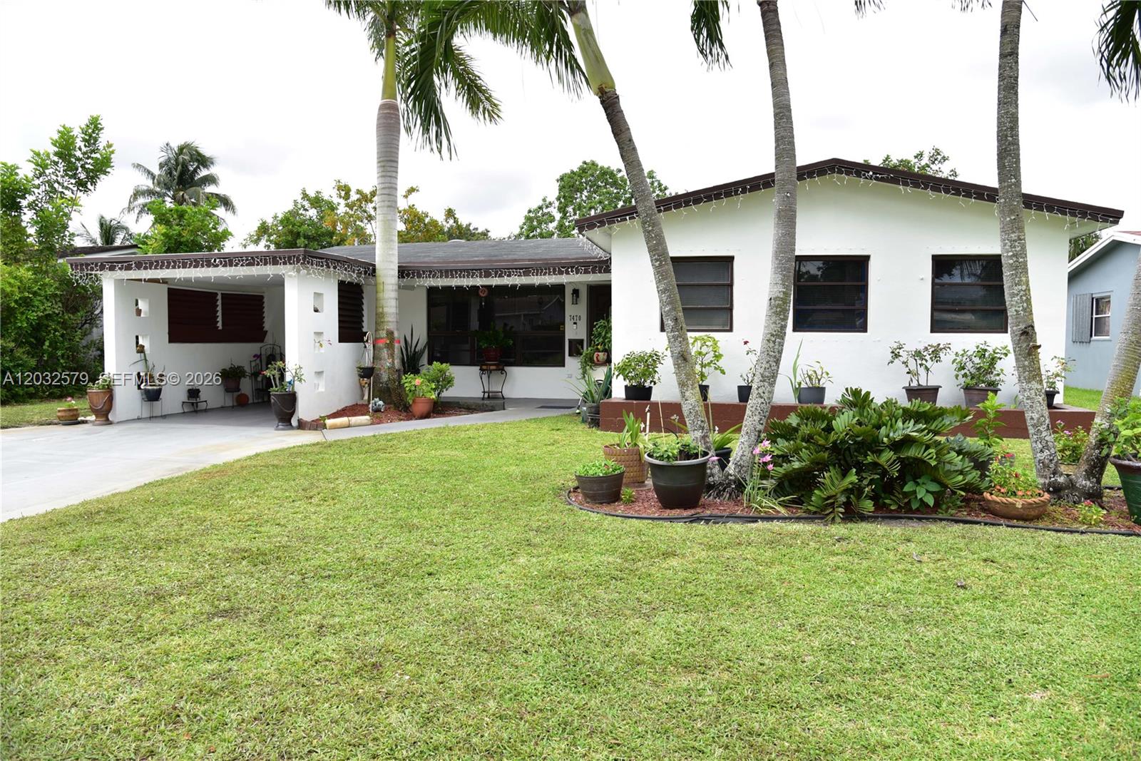 A single-story white house features a carport, palm trees, and a landscaped front yard — 7470 Polk St, Hollywood FL 33024, HOLLYWOOD, FL
