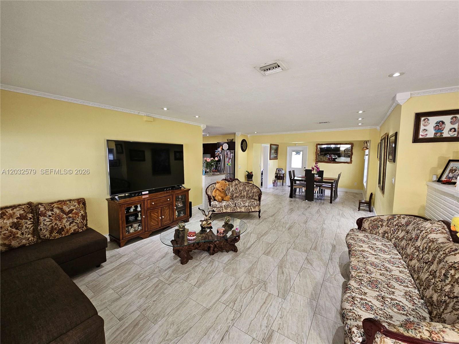 A living room with yellow walls, tile flooring, a large television, and patterned furniture — 7470 Polk St, Hollywood FL 33024, HOLLYWOOD, FL