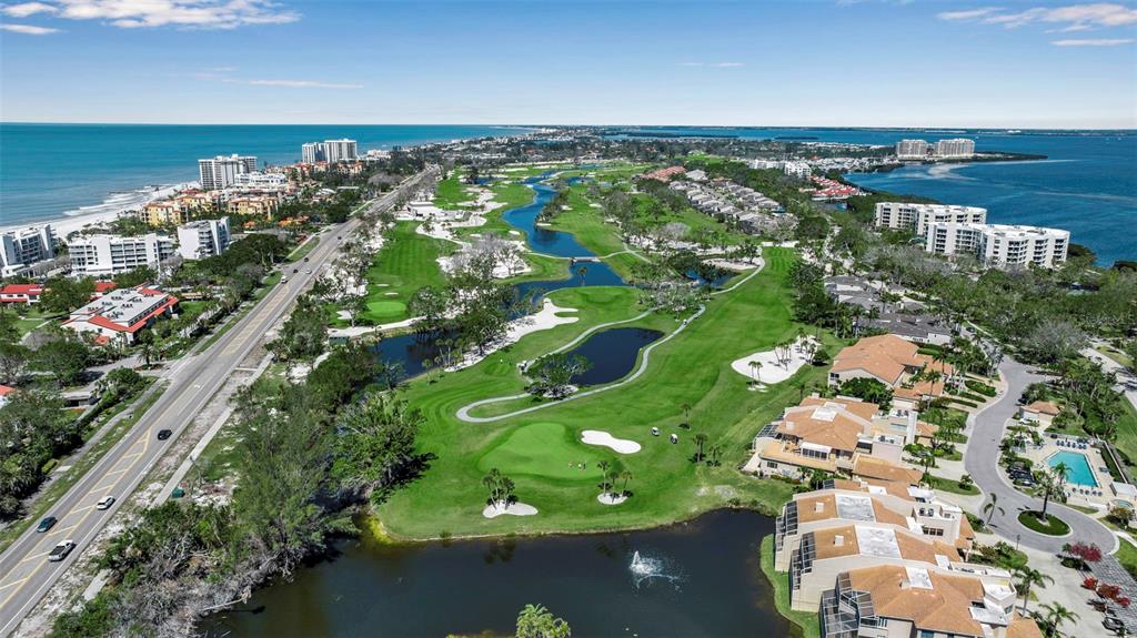 An aerial view shows a golf course situated between a coastal road and residential buildings — 1600 HARBOR SOUND DRIVE, LONGBOAT KEY, FL
