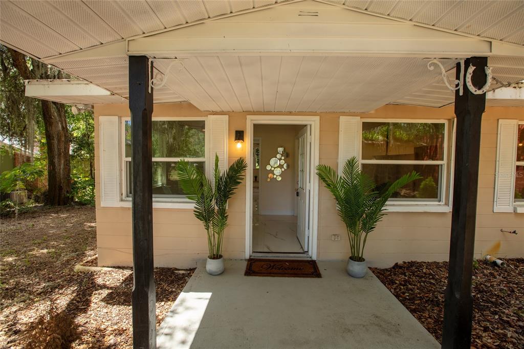 A covered front porch with two potted plants leads to an open entryway — 111 2ND STREET, MELROSE, FL