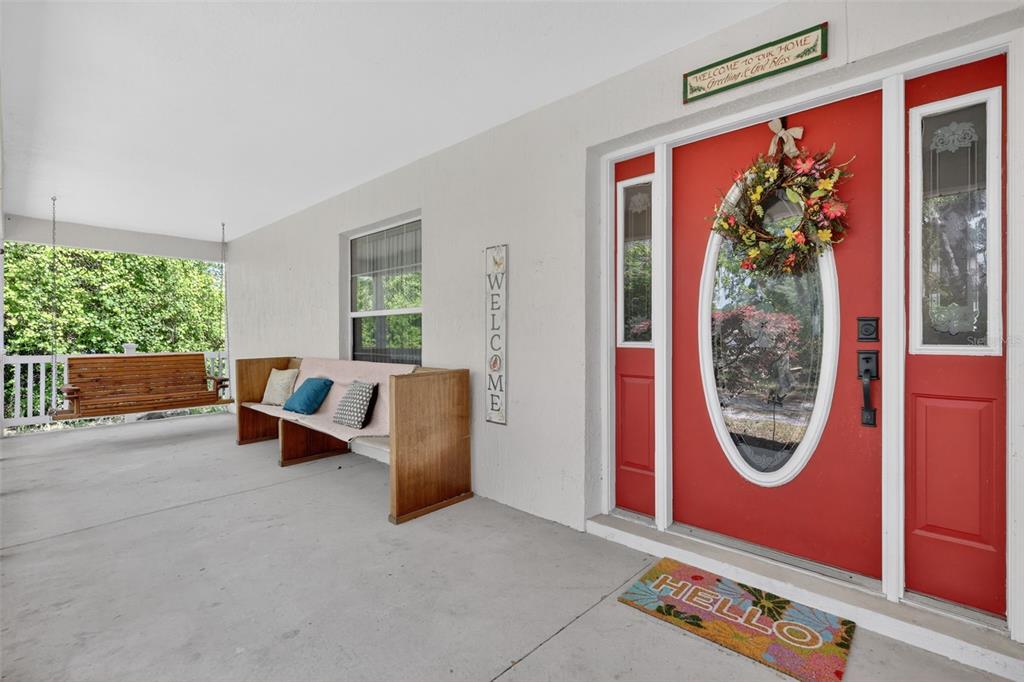A covered porch features a wooden swing, a bench, and a red front door — 41722 POINCIANA STREET, EUSTIS, FL