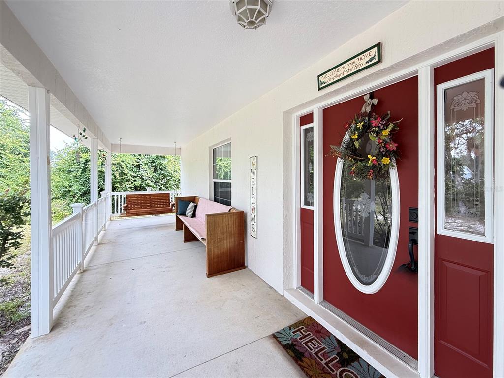 A covered front porch features a wooden bench, a hanging swing, and a red front door — 41722 POINCIANA STREET, EUSTIS, FL