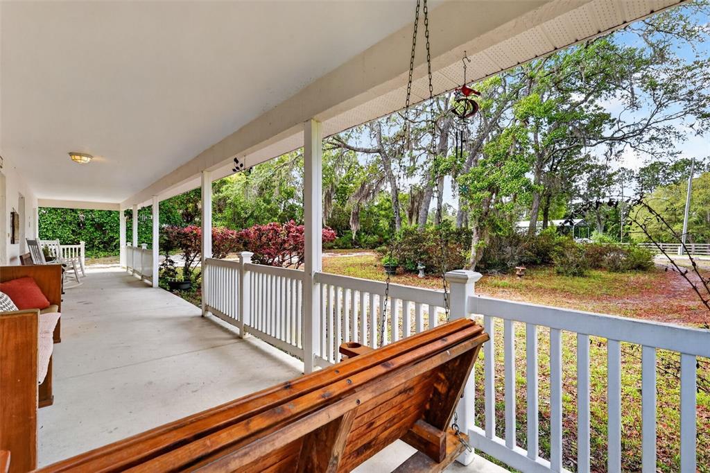 A covered porch features a wooden swing, white railings, and a view of trees — 41722 POINCIANA STREET, EUSTIS, FL