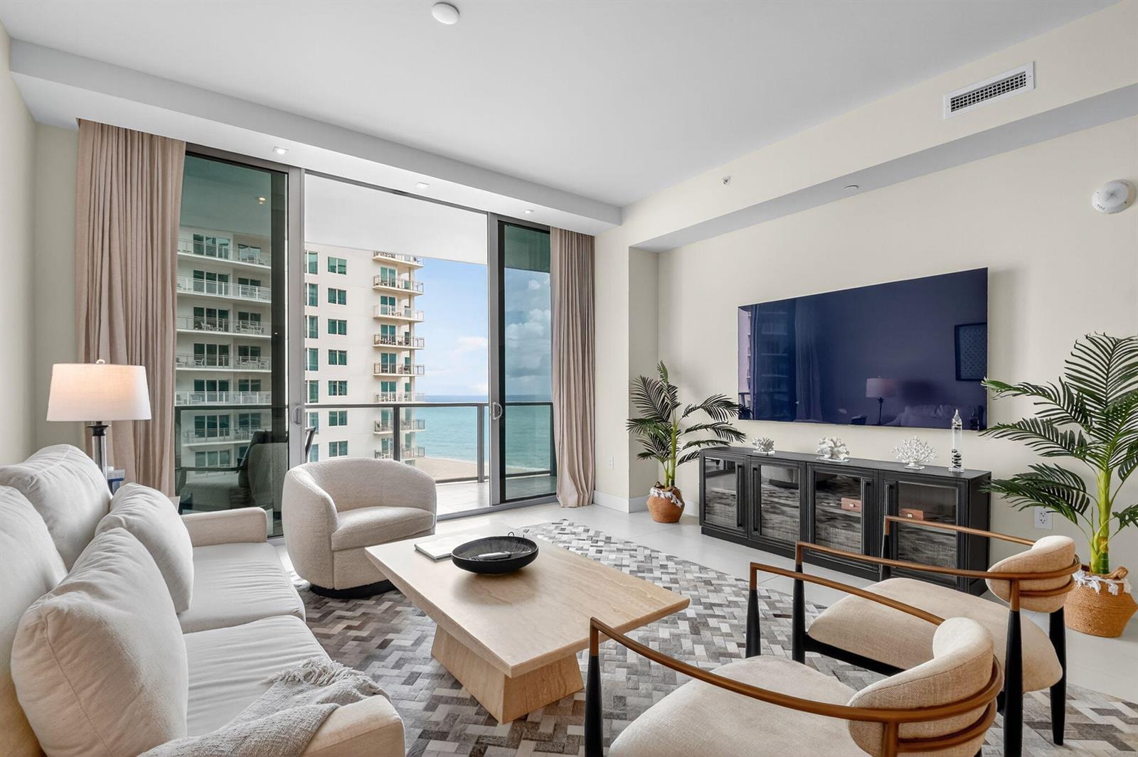 A modern living room features a sofa, armchairs, a television, and a balcony overlooking the ocean — 3100 N Ocean Drive # H, Singer Island FL 33404, SINGER ISLAND, FL