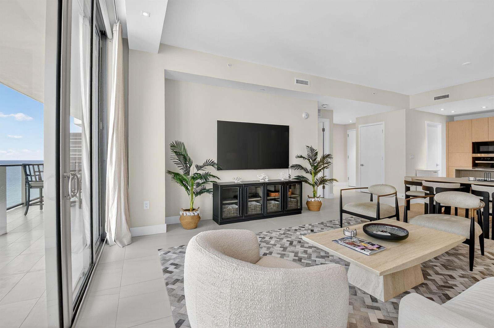 A modern living room features a wall-mounted television, neutral furniture, and a balcony with ocean views — 3100 N Ocean Drive # H, Singer Island FL 33404, SINGER ISLAND, FL