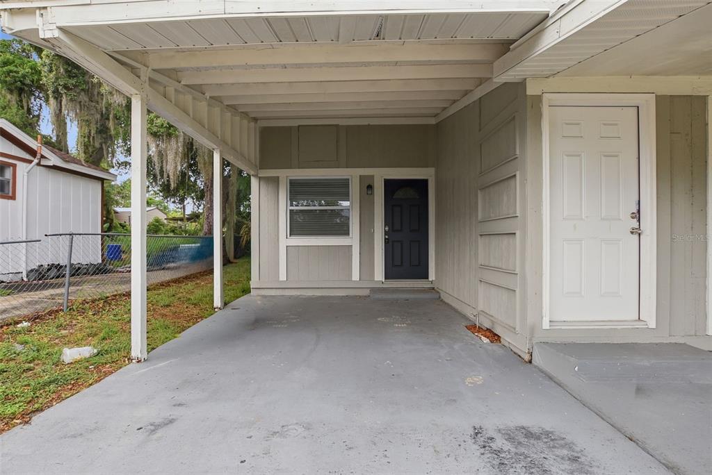 A concrete carport leads to a dark front door and a white side door — 6033 W AMELIA STREET, ORLANDO, FL