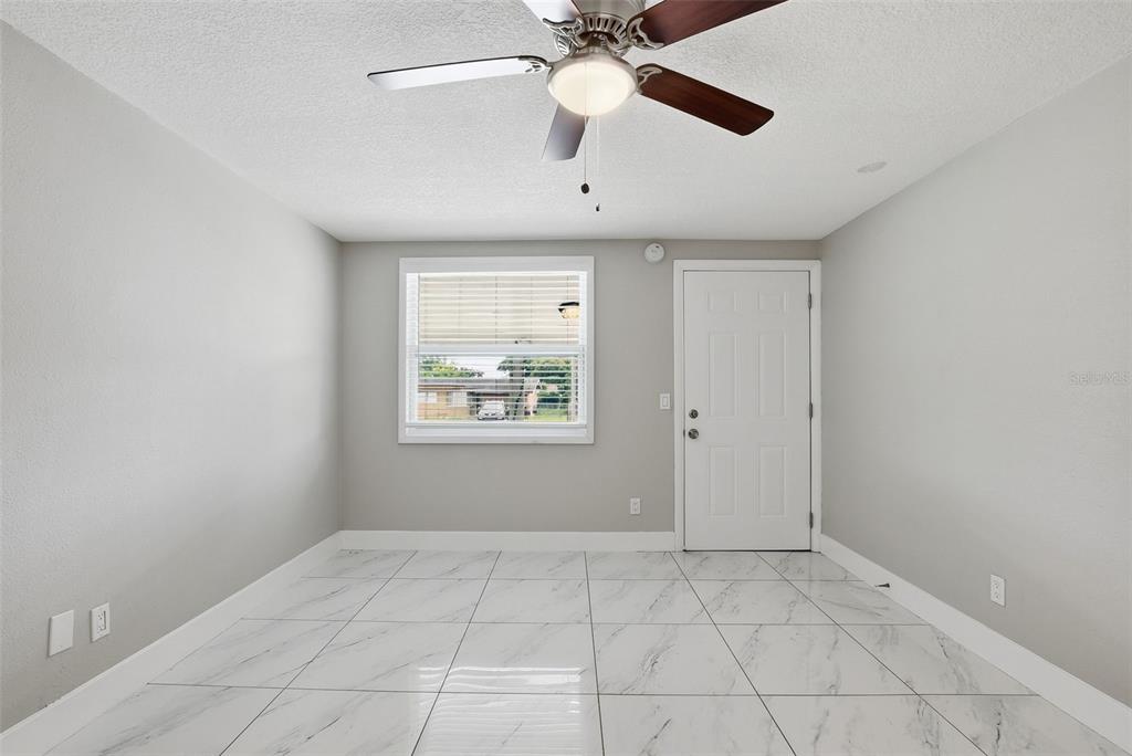 An empty room features white marble-look tile flooring, a ceiling fan, a window, and a door — 6033 W AMELIA STREET, ORLANDO, FL