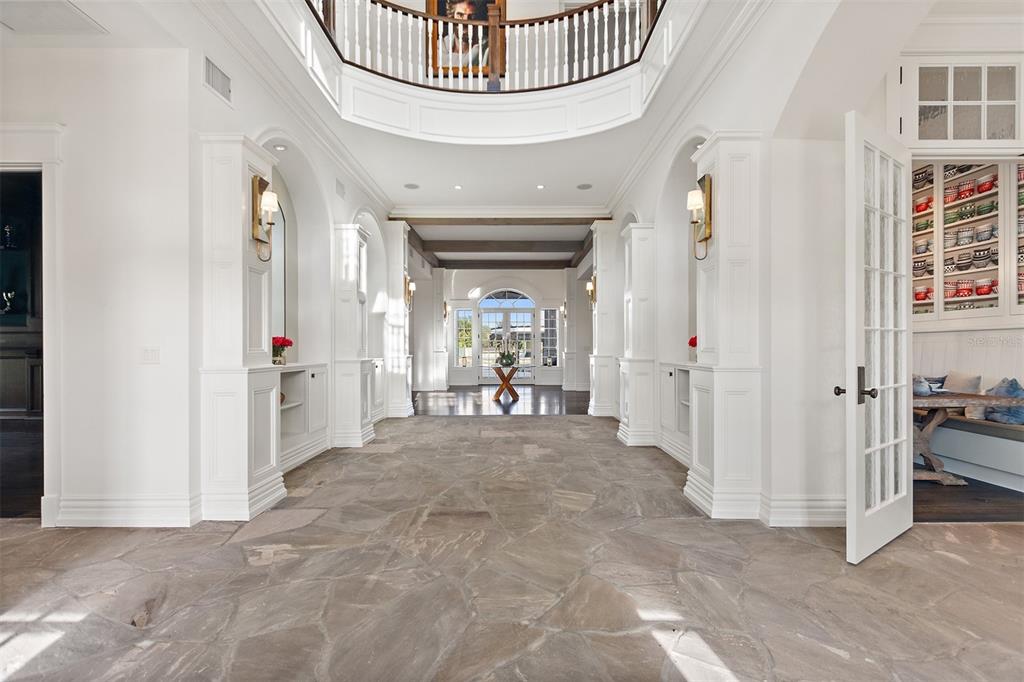 A spacious foyer features stone flooring, white built-in shelving, and a curved second-floor balcony — 3018 KINGFISHER POINT, CHULUOTA, FL