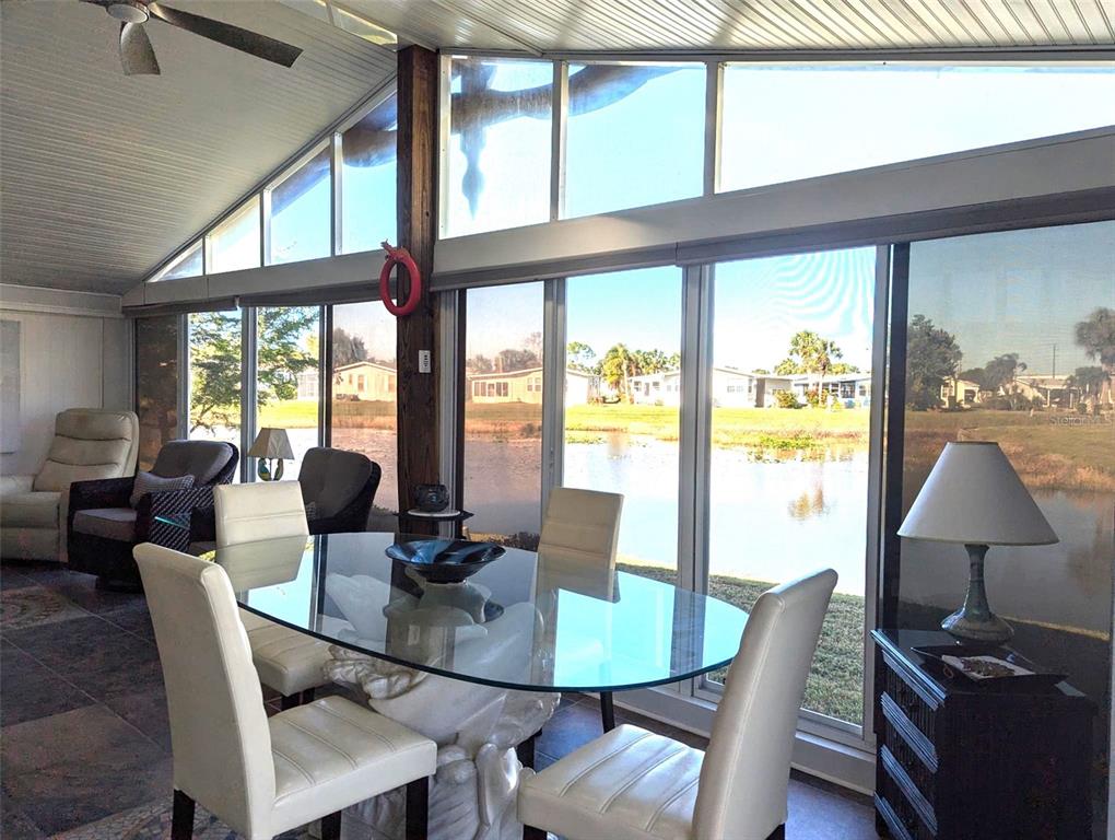 A sunroom with a glass dining table, white chairs, and large windows overlooking a pond — 2100 KINGS HWY UNIT 279, PORT CHARLOTTE, FL