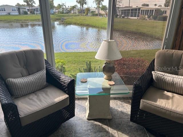 Two wicker armchairs sit on a tiled sunroom floor beside a glass-topped table overlooking water — 2100 KINGS HWY UNIT 279, PORT CHARLOTTE, FL