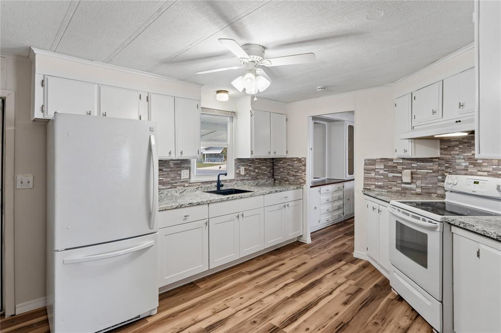 A kitchen features white cabinets, granite countertops, a tiled backsplash, and wood-look flooring — 38552 MONET DRIVE, ZEPHYRHILLS, FL