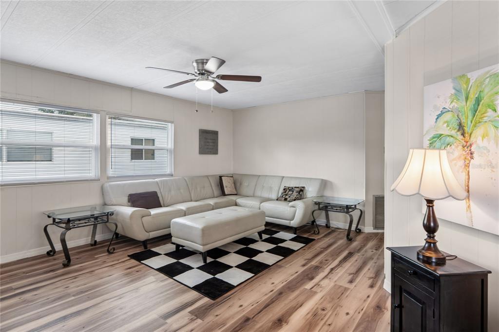 A living room features a white sectional sofa, a checkered rug, and wood-look flooring — 38552 MONET DRIVE, ZEPHYRHILLS, FL