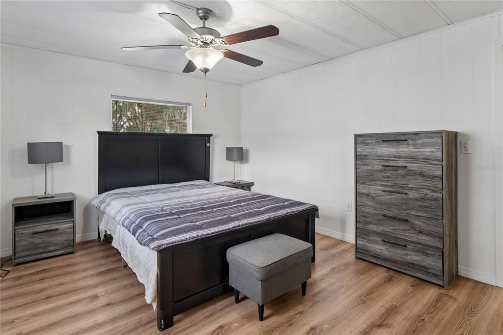A bedroom features a black bed frame, a gray dresser, and wood-look flooring — 38552 MONET DRIVE, ZEPHYRHILLS, FL