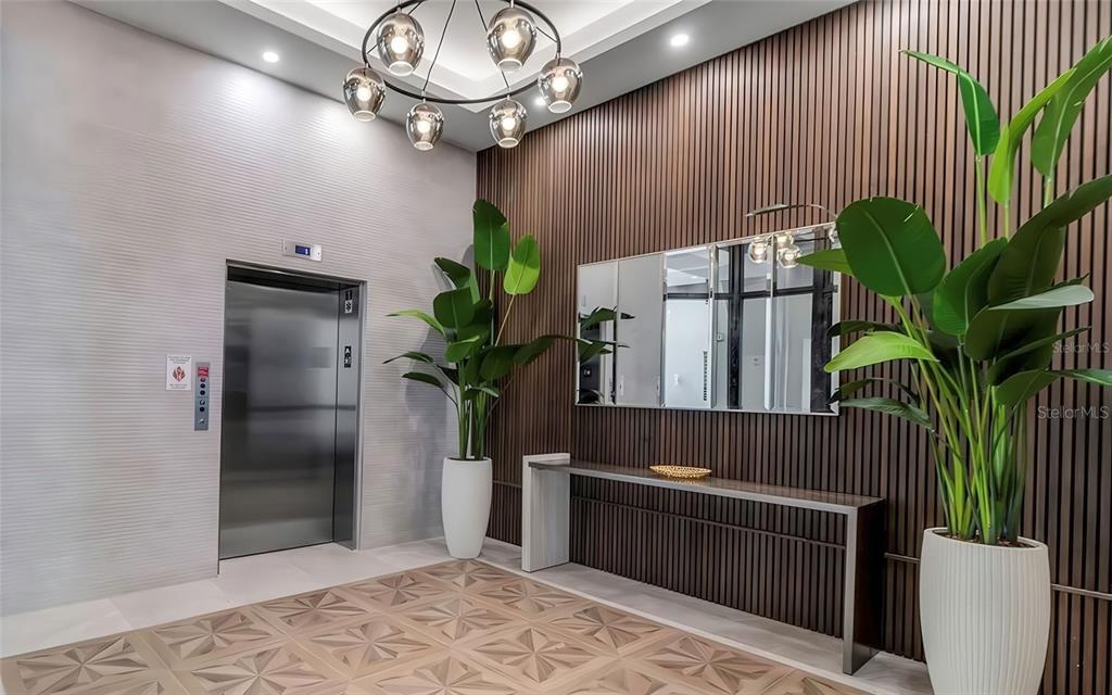 A modern elevator lobby features wood-slat walls, a geometric patterned floor, and two large potted plants — 33 S PALM AVENUE UNIT 1501, SARASOTA, FL