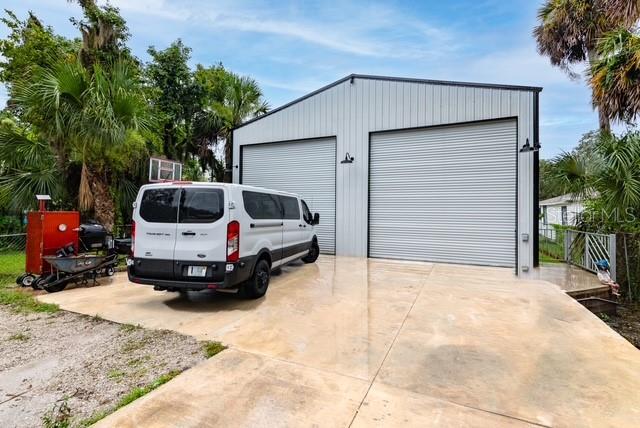 A white metal workshop building with two roll-up doors sits on a concrete driveway — 334 SHELDON STREET, NEW SMYRNA BEACH, FL