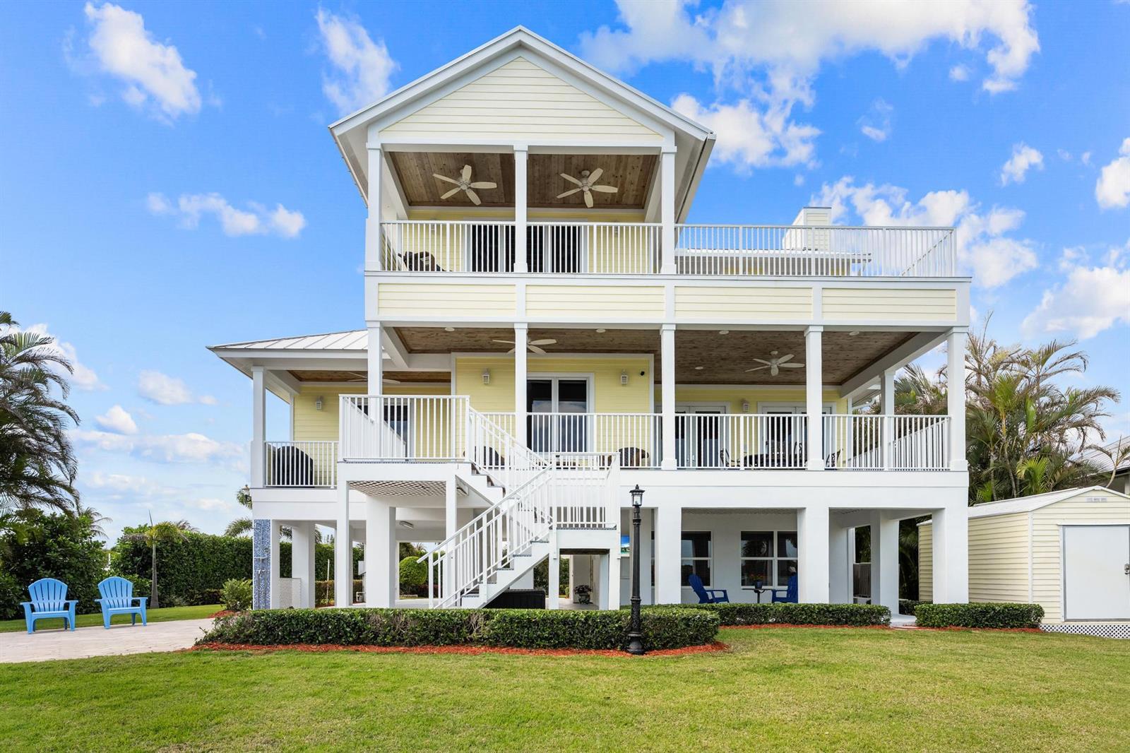 A three-story yellow house on stilts features white railings, a staircase, and a grassy yard — 5675 SE Orange Street, Stuart FL 34997, STUART, FL