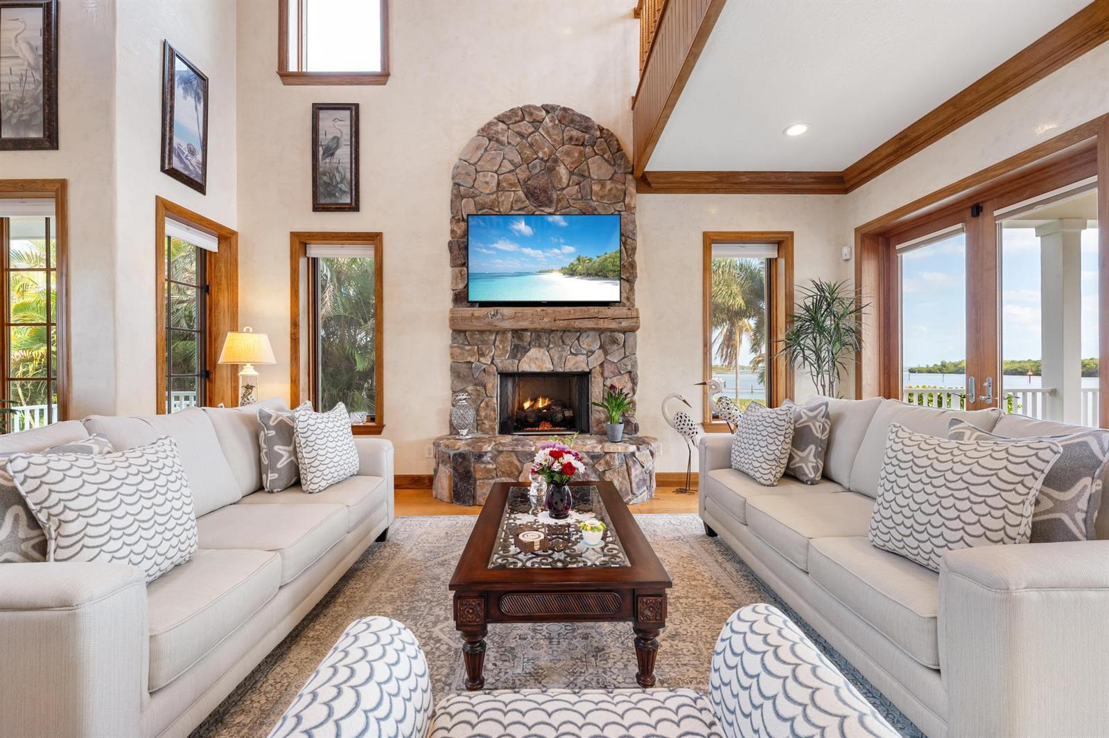 A living room features a stone fireplace, two sofas, and large windows with water views — 5675 SE Orange Street, Stuart FL 34997, STUART, FL