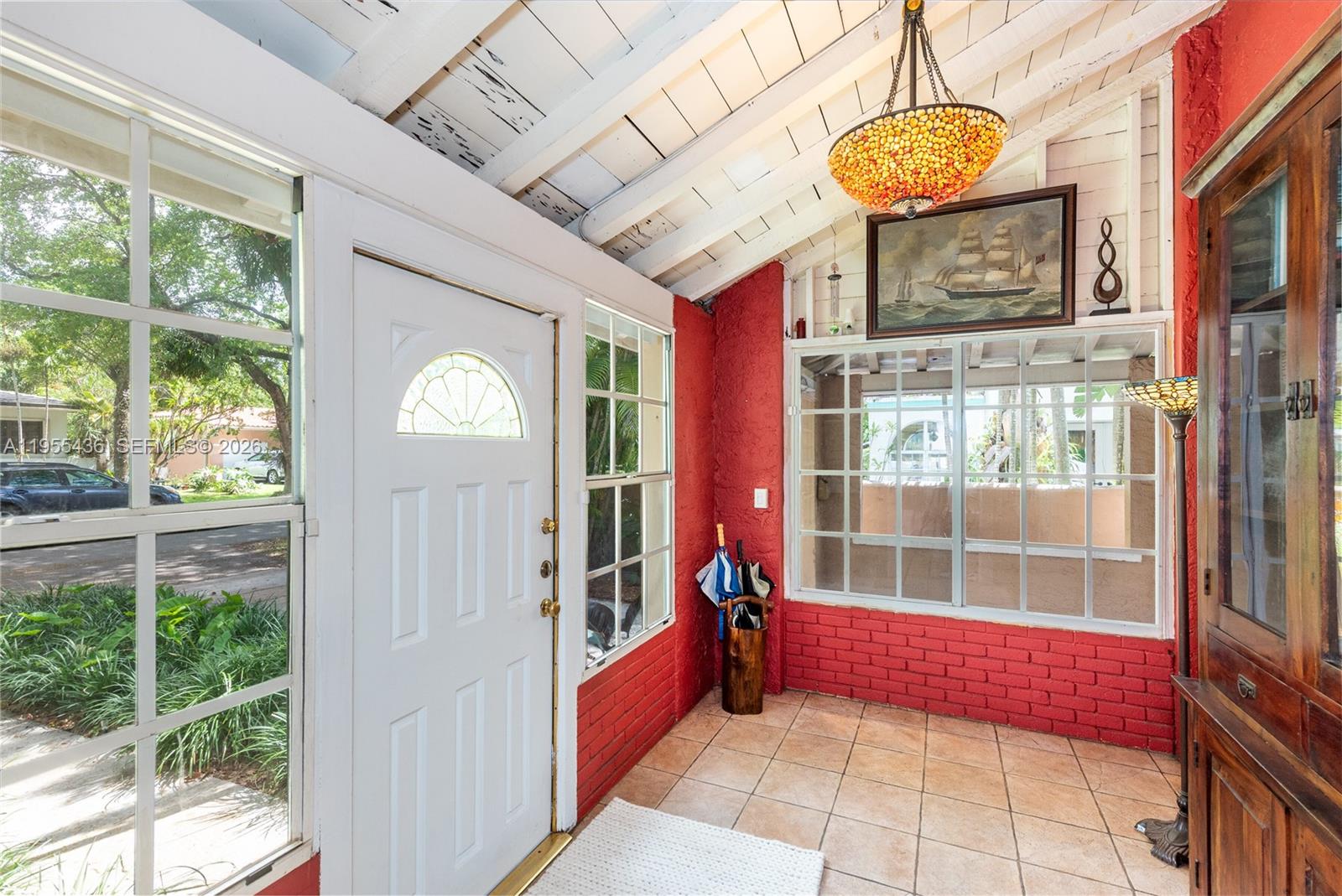 A sunroom features red brick walls, tile flooring, a white door, and a hanging lamp — 1256 Algeria Ave, Coral Gables FL 33134, CORAL GABLES, FL