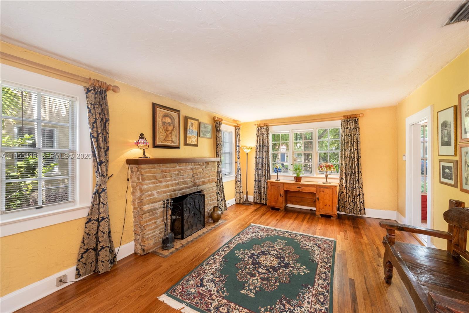 A living room features yellow walls, a stone fireplace, hardwood floors, and a patterned rug — 1256 Algeria Ave, Coral Gables FL 33134, CORAL GABLES, FL