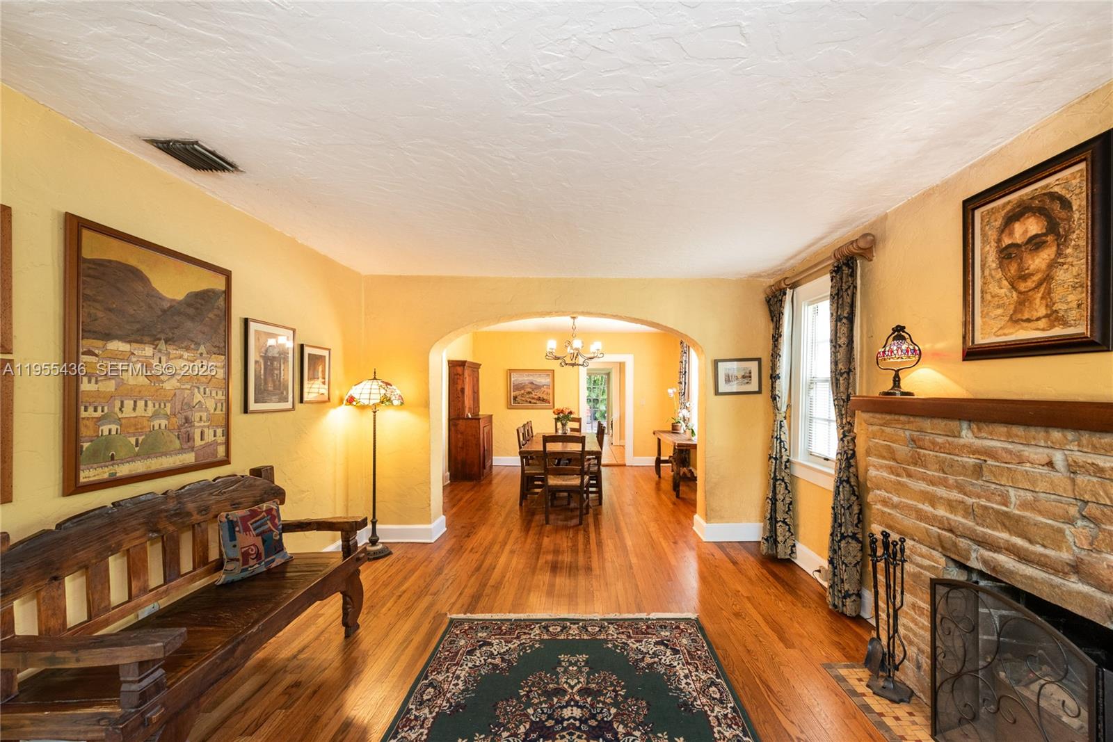 A living room with a stone fireplace, hardwood floors, and an arched entryway to dining — 1256 Algeria Ave, Coral Gables FL 33134, CORAL GABLES, FL