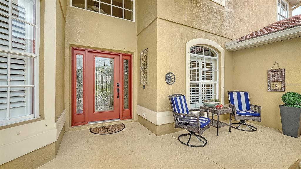 A covered entryway features a red front door, two patio chairs, and a small table — 116 NEW BRITON COURT, BRADENTON, FL