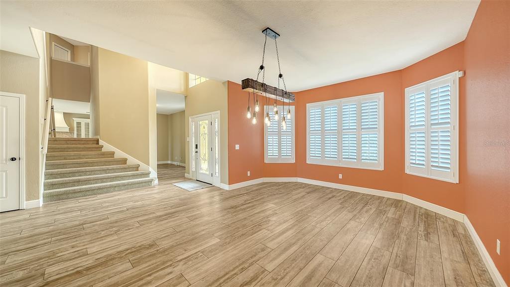 A dining room with wood-look tile flooring, a rustic chandelier, and orange accent walls — 116 NEW BRITON COURT, BRADENTON, FL