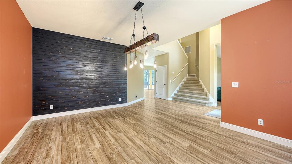 A dining room features a dark wood-plank accent wall, wood-look tile flooring, and a chandelier — 116 NEW BRITON COURT, BRADENTON, FL