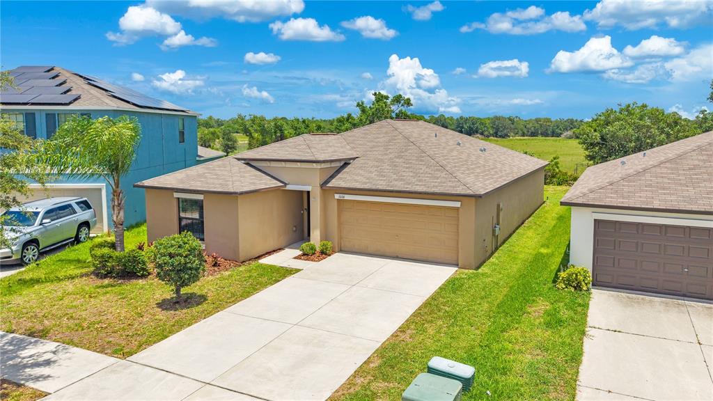 An exterior view of a tan, single-story suburban house with a two-car garage — 10116 CARLOWAY HILLS DRIVE, WIMAUMA, FL