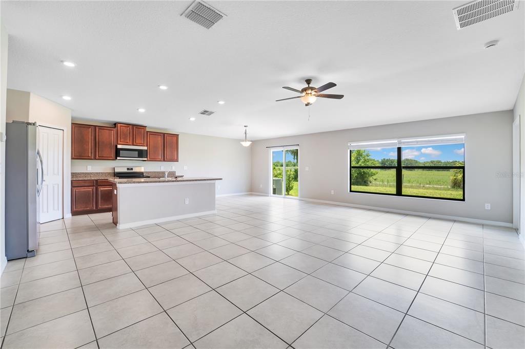 An open-concept kitchen and living area with tile flooring, dark wood cabinets, and large windows — 10116 CARLOWAY HILLS DRIVE, WIMAUMA, FL