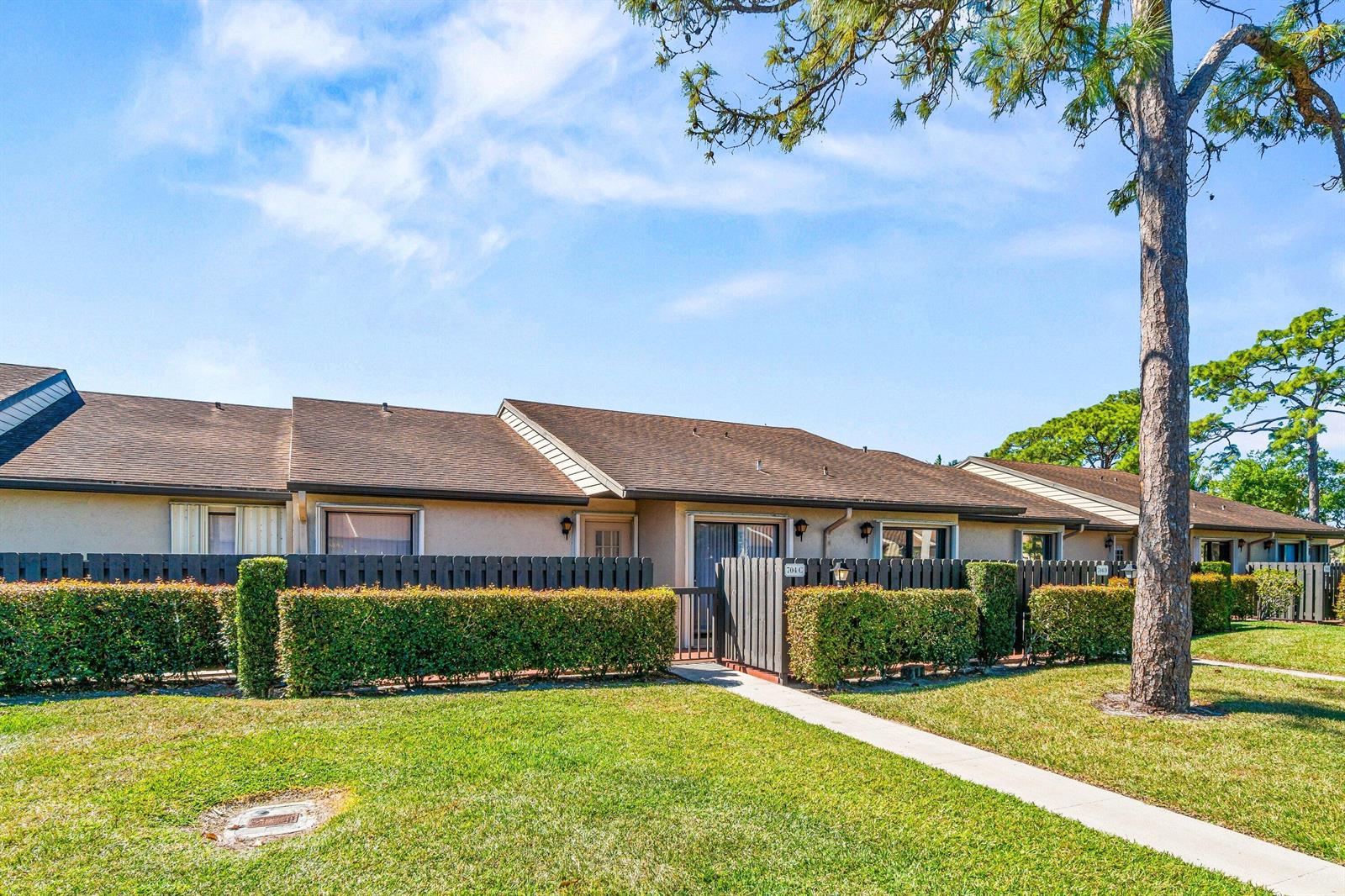 A single-story residential building with a brown roof, tan exterior, and a fenced-in patio area — 704 Sunny Pine Way # C, FL 33415, FL