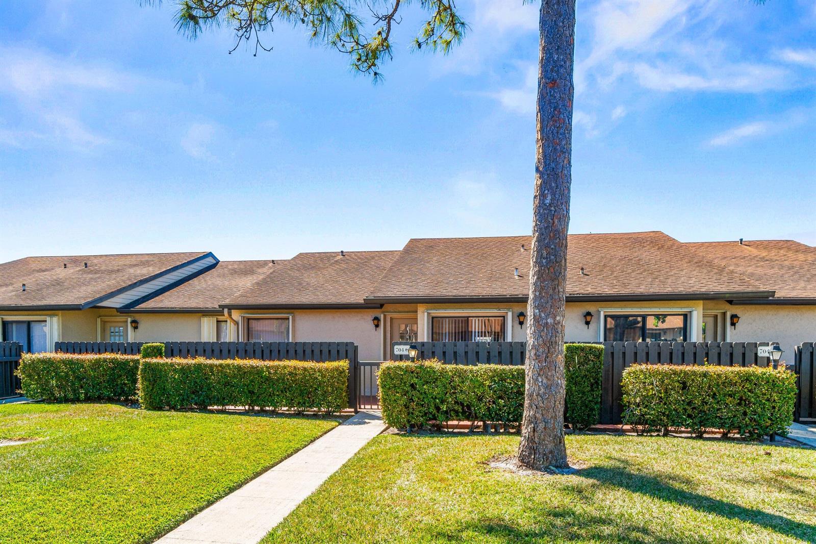 A single-story residential building with a brown roof, tan exterior, and a fenced front patio — 704 Sunny Pine Way # C, FL 33415, FL