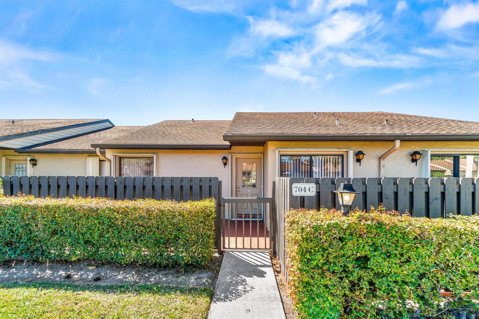 A single-story residential unit with a gated courtyard, hedge, and a concrete walkway — 704 Sunny Pine Way # C, FL 33415, FL
