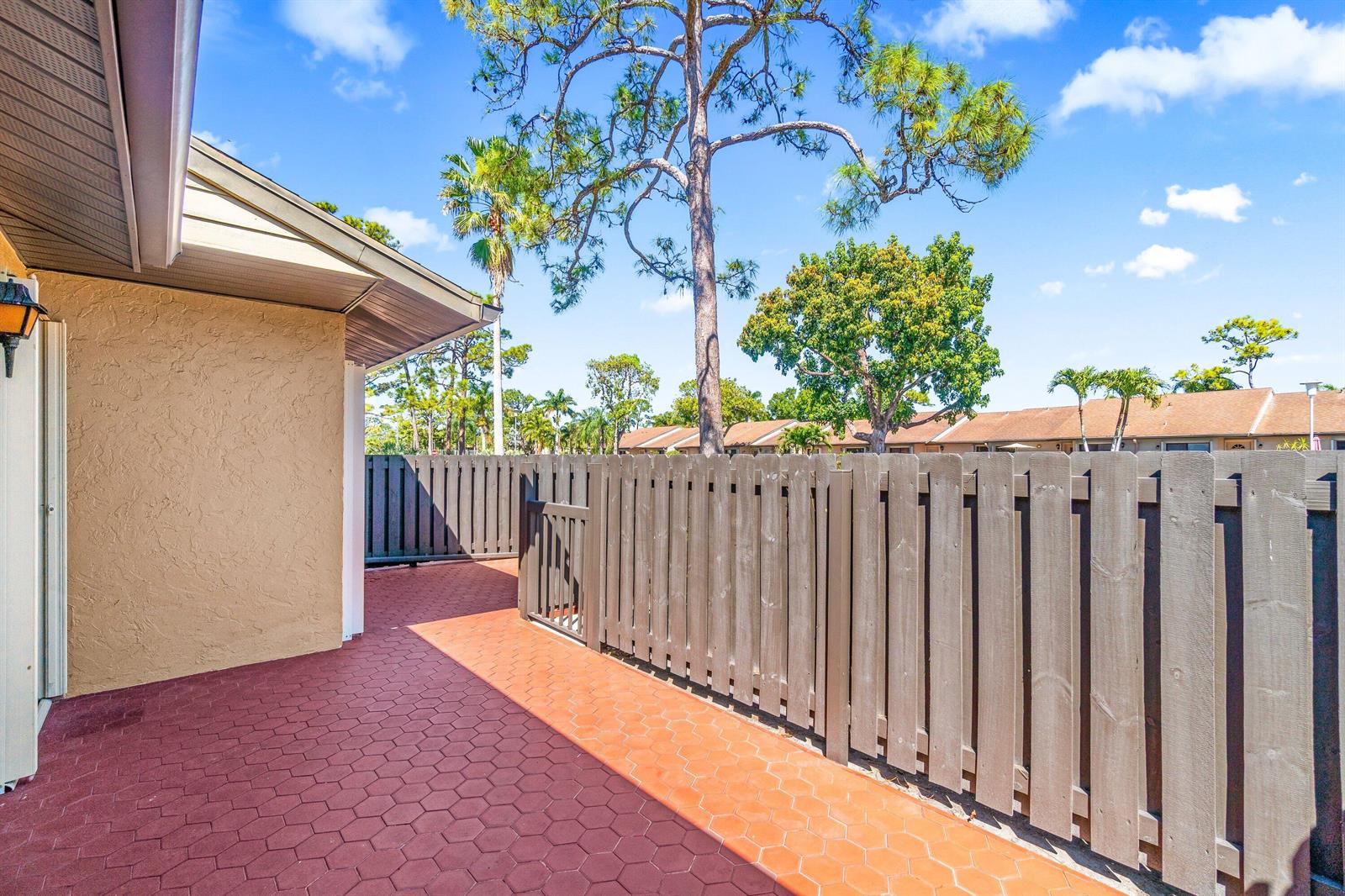 A red-tiled patio sits beside a beige house wall and a wooden privacy fence — 704 Sunny Pine Way # C, FL 33415, FL