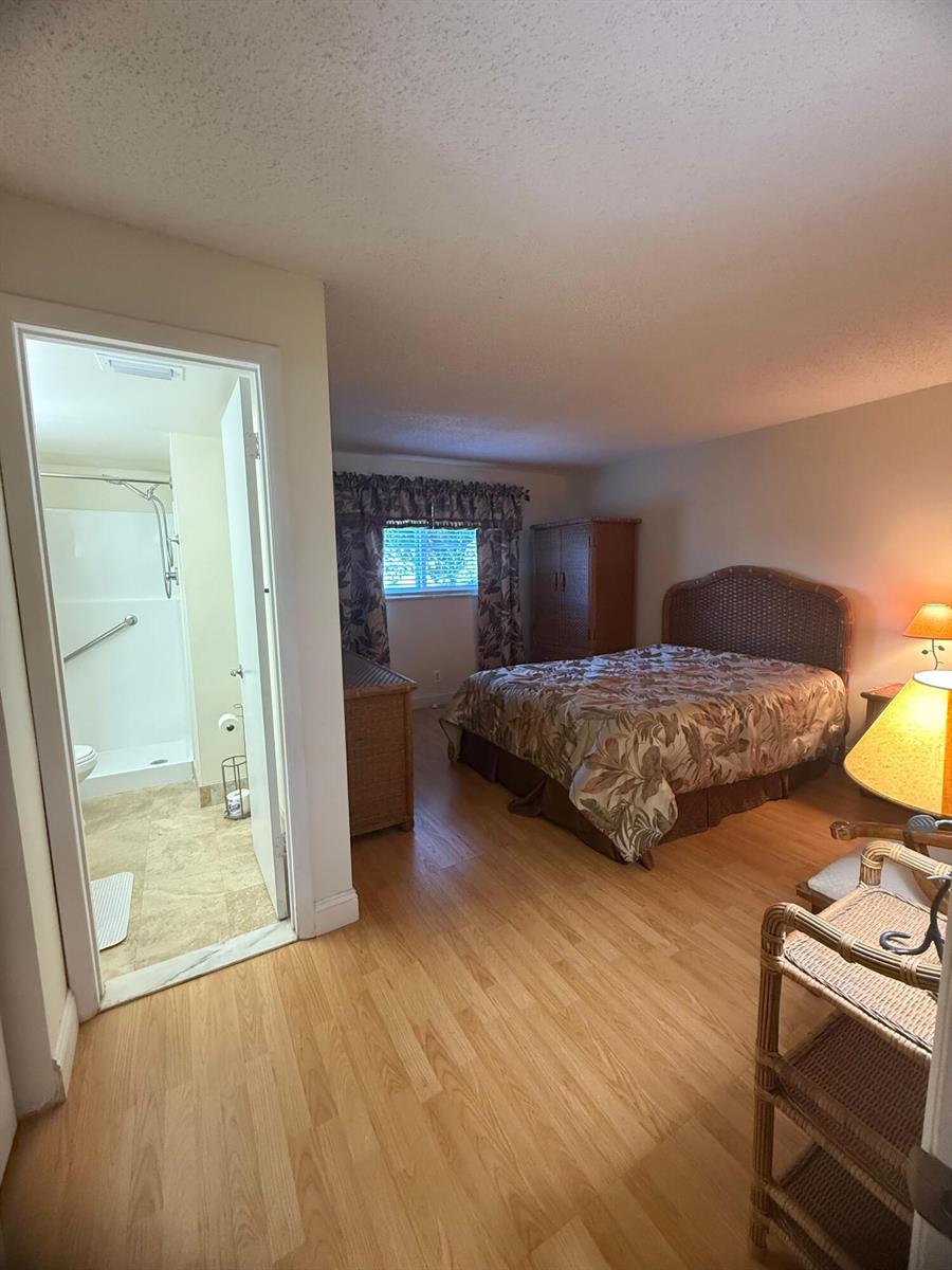 A bedroom with wood-look flooring, a wicker headboard, and an attached bathroom with a shower — 2601 NE 3rd Court # 202, Boynton Beach FL 33435, BOYNTON BEACH, FL
