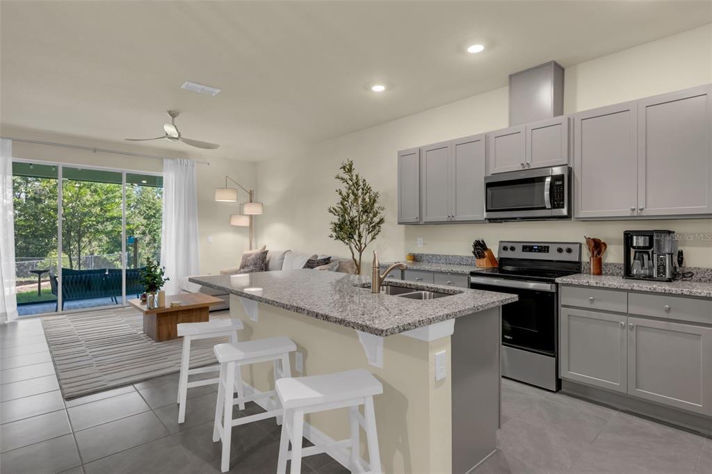 A kitchen with gray cabinets and granite countertops overlooks a living area with sliding doors — 1219 LIDO DRIVE, HOWEY IN THE HILLS, FL