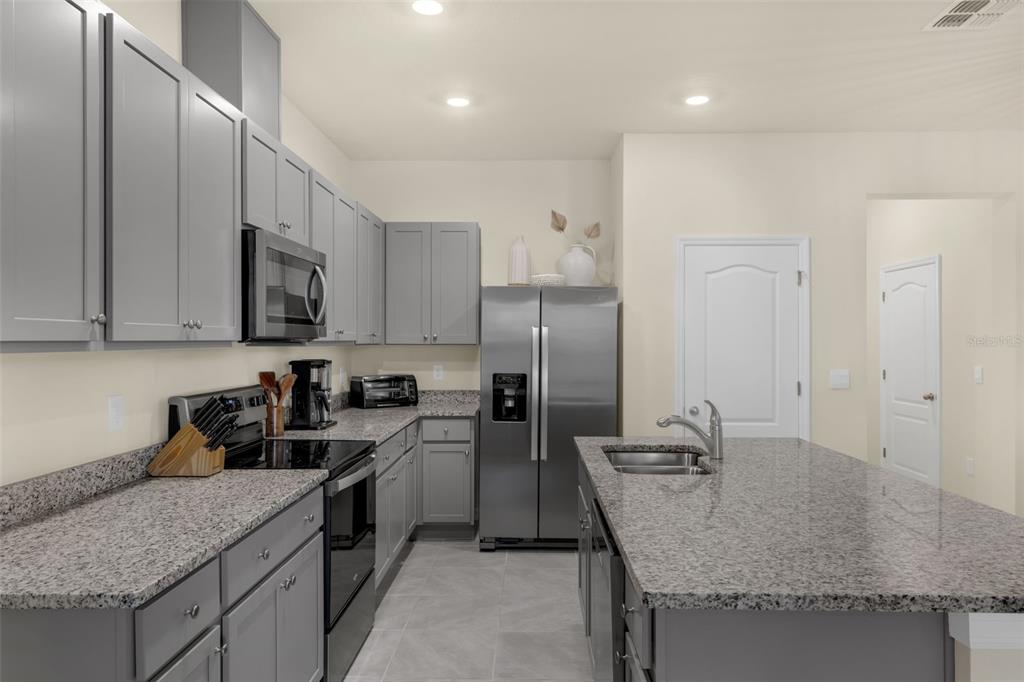A kitchen features gray cabinets, granite countertops, stainless steel appliances, and a central island — 1219 LIDO DRIVE, HOWEY IN THE HILLS, FL