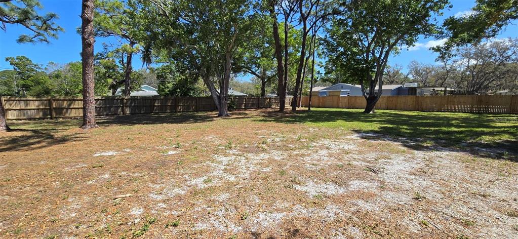 A large, partially shaded backyard features a wooden privacy fence and scattered patches of grass — 13296 98TH AVENUE N, SEMINOLE, FL