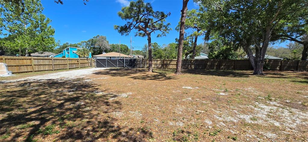 A fenced, grassy lot features scattered trees and a gravel driveway leading to a gate — 13296 98TH AVENUE N, SEMINOLE, FL