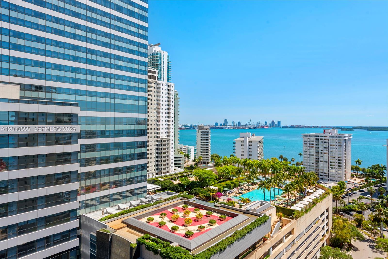 An elevated view shows a high-rise building overlooking a swimming pool, lush landscaping, and the ocean — 1451 Brickell Ave # 1706, Miami FL 33131, MIAMI, FL