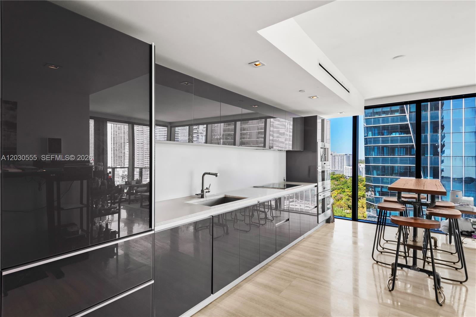 A modern kitchen features high-gloss grey cabinetry, stone countertops, and floor-to-ceiling windows with city views — 1451 Brickell Ave # 1706, Miami FL 33131, MIAMI, FL