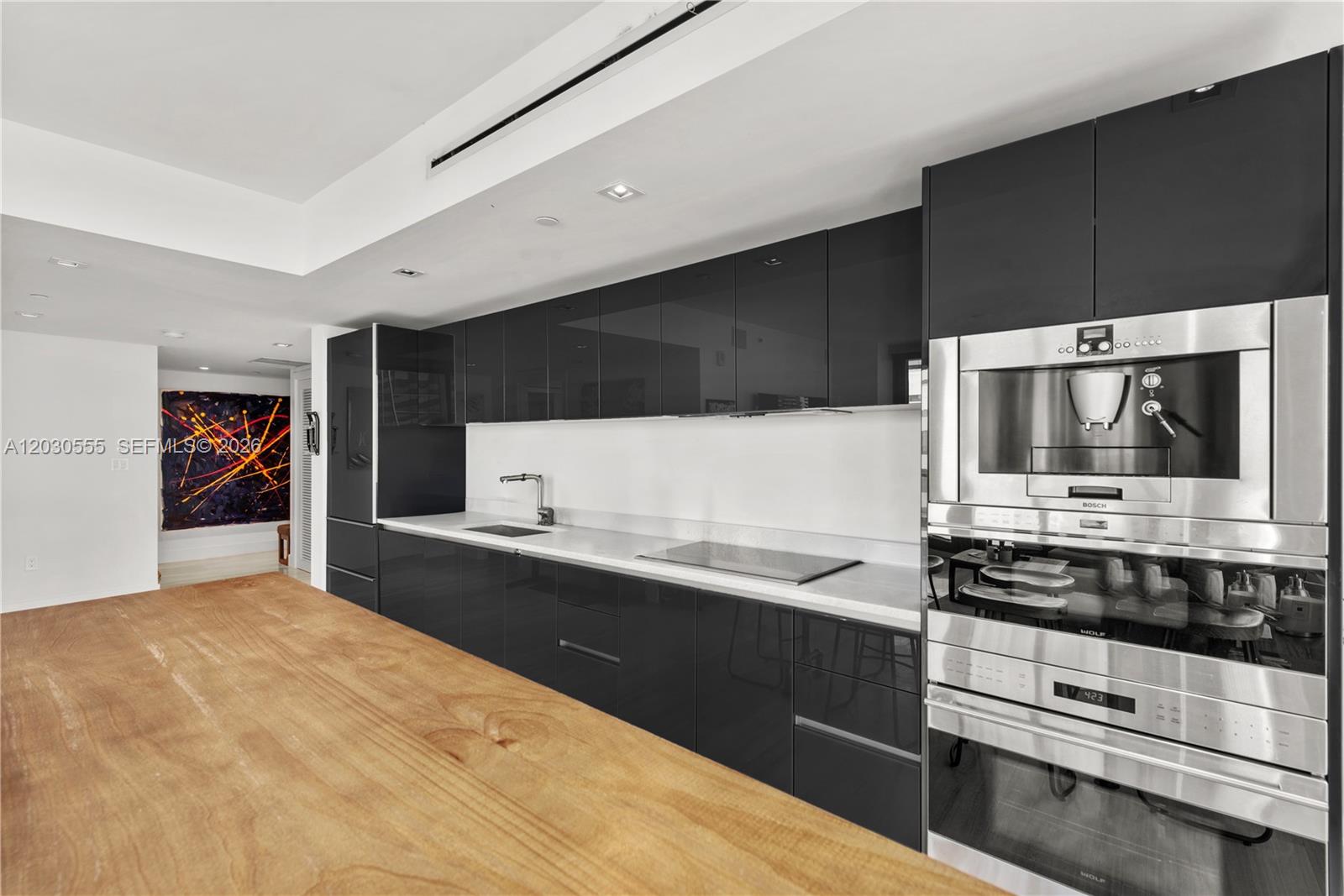 A modern kitchen features glossy black cabinetry, a wooden island, and stainless steel built-in appliances — 1451 Brickell Ave # 1706, Miami FL 33131, MIAMI, FL