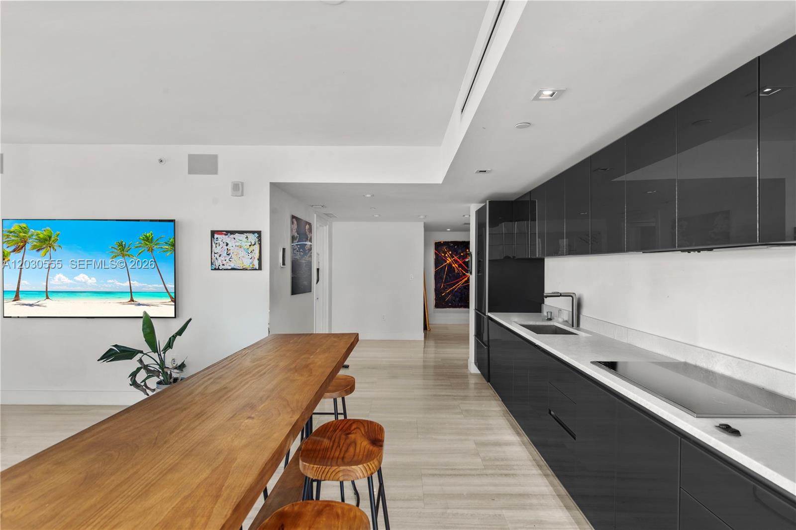 A modern kitchen features dark cabinetry, a white countertop, and a long wooden dining table — 1451 Brickell Ave # 1706, Miami FL 33131, MIAMI, FL