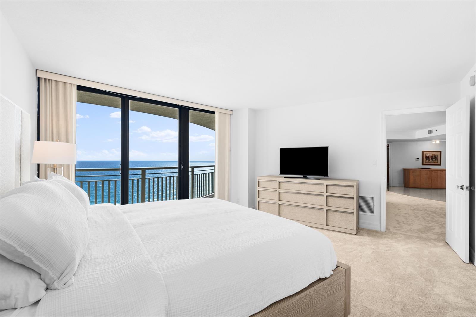 A bedroom features a king bed, a dresser with a television, and a balcony view — 3000 N Ocean Drive # 28e, Riviera Beach FL 33404, RIVIERA BEACH, FL