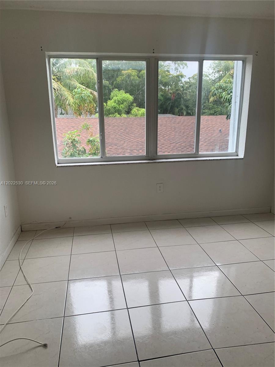 An empty room features white tiled floors, plain walls, and a large window overlooking trees — 1090 NE 129th St # 202, North Miami FL 33161, NORTH MIAMI, FL